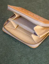 Billetera de cuero color tostado con cierre de cremallera. Interior con seis compartimentos para tarjetas y un compartimento para monedas con cierre. El billete entra doblado.