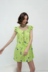 Vestido corto color verde lima con estampado de cerezas y otros dibujos en azul. Tiene escote cuadrado con volados en los hombros y lazos ajustables en el frente.