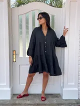 Vestido corto negro de lino, con escote en V, botones frontales y mangas largas acampanadas con volados.