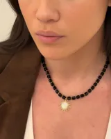 Collar corto de cuentas facetadas negras con detalles dorados y dije de sol dorado con centro de circonias.