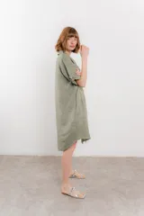 Vestido camisero corto color verde oliva, confeccionado en lino 100%. Tiene botones en la parte delantera, cuello camisero, mangas cortas con botón para arremangar y bolsillos laterales.