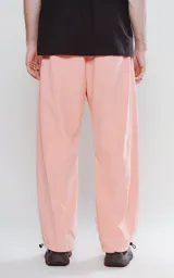 Pantalón de corte sastrero color salmón, de tela suede suave y holgada, con bolsillos laterales, cintura trasera elástica ajustable y cierre frontal con botón.
