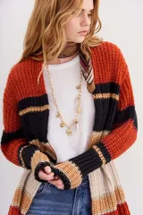 Cárdigan tejido de calce holgado, mangas largas y diseño a rayas horizontales en tonos naranja, negro, beige y blanco.