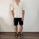 Camisa negra tejida con diseño calado, corte regular, cuello tipo polo y cierre frontal con botones.