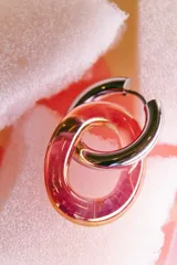 Par de aros tipo argolla con forma de dona, uno plateado y otro rosa con efecto cromado.