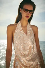 Vestido corto de cuello halter y escote fluido, color dorado, con lentejuelas y forro interior. Cierre lateral con cremallera oculta en costura.