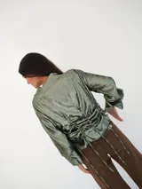 Camisa verde esmeralda con reflejos tornasolados, de corte holgado, con cuello camisero, cierre frontal con botones de nácar y mangas largas con puños abotonados.