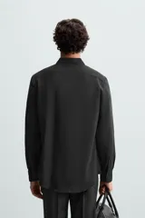 Camisa negra de manga larga, corte slim fit, con cuello italiano y cierre frontal de botonadura.