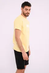 Remera mostaza de algodón con cuello redondo y estampado de una bicicleta con tablas de surf y el texto "Live Simply".