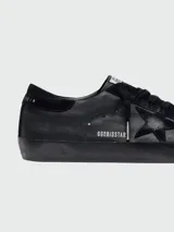 Zapatillas urbanas Golden Goose modelo Super-Star para hombre, confeccionadas en cuero napa color negro. Presentan el icónico parche de estrella en el lateral, inscripción 'GGDB/SSTAR' y suela de goma con efecto desgastado.