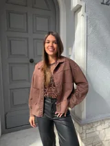 Chaqueta marrón de gamuza con cuello camisero, cierre frontal con botones y bolsillos de parche en el pecho.