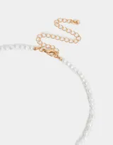 Collar corto con perlas blancas irregulares y dijes colgantes dorados: cristal amatista, rectángulo de nácar, corazón de nácar y dije circular con diseño de corazón y rayos.