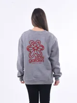 Buzo de tejido de punto color gris melange, con cuello redondo y manga larga. Presenta un estampado frontal en rojo que incluye una flor estilizada y el texto "slow garden there's no hurry".