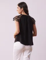 Blusa negra de crepe con apliques de crochet en los hombros. Tiene cuello redondo, mangas cortas y espalda con abertura ojal y botones.