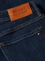 Jeans de calce ajustado color azul oscuro, con diseño de cinco bolsillos, cierre de botón y cremallera, detalles distintivos de Tommy Hilfiger, logo sobre el bolsillo posterior y parche en la cintura.