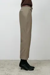 Pantalón de vestir color beige, de tiro alto y corte recto. Incluye cinturón marrón con hebilla metálica. Presenta bolsillos laterales y falsos bolsillos traseros de doble vivo. Cierre frontal con cremallera, botón interior y gancho oculto.