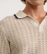 Camisa polo de manga corta, color beige claro, con textura de tejido abierto tipo ganchillo. Posee cuello y ribetes en las mangas en color azul marino.