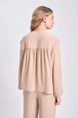 Blusa color beige de manga larga, con cuello en V y cierre frontal con botones.
