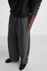 Pantalón jogger wide fit color gris oscuro, confeccionado en tejido de algodón compacto con elasticidad. Cuenta con cintura elástica ajustable con cordón, pliegues frontales, bolsillos delanteros y bolsillo trasero de parche.