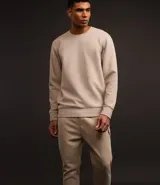 Conjunto deportivo color beige compuesto por un buzo de cuello redondo y un pantalón de jogging con cintura elástica y bolsillos laterales. El buzo es de corte clásico y el pantalón es ajustado en los tobillos.