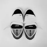 Zapatillas bajas de gamuza negra con detalles en cuero sintético blanco y suela de goma blanca.