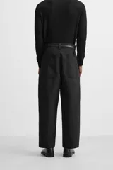 Pantalón negro de corte amplio tipo balloon fit, con cintura con pliegues frontales, bolsillos delanteros y traseros de plastrón. Cierre frontal con cremallera y botón.