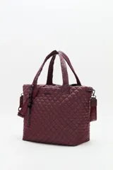 Bolso tote grande acolchado color vino tinto, con costuras en patrón de rombos. Posee dos asas de mano y una correa ajustable y desmontable con texto repetido. Incluye un charm colgante con letras negras.