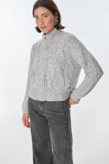 Cardigan color crudo de tejido de punto con diseño trenzado, cuello alto y cierre frontal con cremallera.