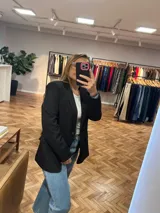 Blazer negro de corte clásico con solapas de muesca, cierre frontal con dos botones y bolsillos laterales con solapa.