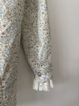 Camisa blanca estampada con flores pequeñas en tonos celeste, rosa y amarillo. Confeccionada en lino 100%, con botones de nácar y puntilla de algodón en los puños.