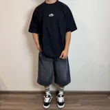 Remera color crudo de corte oversize y mangas cortas, con estampa en la espalda de una mano alcanzando un círculo.