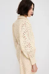 Vestido corto color beige con broderie, cuello camisero, botonadura frontal, cinturón extraíble con hebilla redonda, mangas globo largas con puños abotonados y ribetes festoneados.