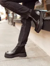 Botines negros de cuero con caña baja, puntera redondeada y cierre frontal con cremallera. Presentan paneles laterales de gamuza y suela track con plataforma.