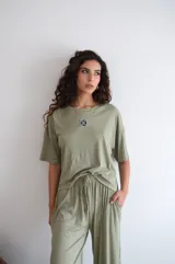 Conjunto de dos piezas color crema, compuesto por una remera de mangas cortas con logo bordado en el pecho y un pantalón palazzo con cintura elastizada y cordón ajustable.