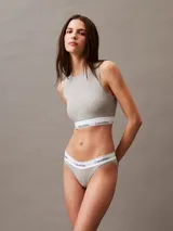 Conjunto Calvin Klein Modern Cotton color gris melange, compuesto por un corpiño deportivo sin mangas y una bombacha tipo tanga, ambos con banda elástica blanca con logo de la marca.