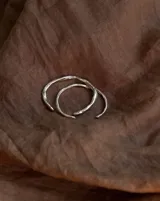 Brazalete rígido abierto de metal color plateado con textura irregular.