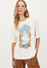 Camiseta color beige de corte amplio con estampado de un paisaje costero enmarcado por una estructura arquitectónica y la frase "Blue Horizon".
