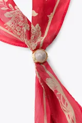 Pañuelo bandana de seda color rojo con estampado floral en dorado y cierre ajustable con pieza metálica y aplicación de piedra.