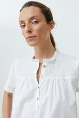 Blusa blanca con punto smock en el cuello, manga corta y cierre con botones.