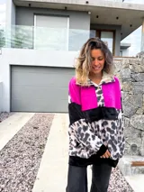 Buzo de corte amplio con bloques de color fucsia, negro y estampado animal print de leopardo en tonos beige y negro. Tiene cuello alto con cierre de botones a presión y bolsillo tipo canguro con botones a presión.