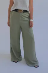 Pantalón verde oliva de corte palazzo, con cintura alta y pernera ancha. Incluye cinturón trenzado negro con hebilla metálica decorada.