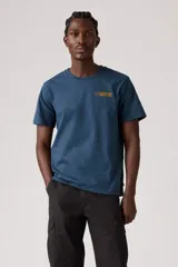 Remera de manga corta, cuello redondo, color azul oscuro, con un pequeño parche gráfico rectangular con texto en tono mostaza en el pecho.