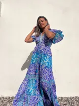Vestido largo de seda con estampado paisley en tonos turquesa, azul y blanco. Tiene escote en V, mangas cortas con volados y talle imperio con cordón ajustable.