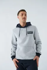 Buzo canguro gris con capucha ajustable y bolsillo delantero. Tiene puños y cintura acanalados en azul marino, y un parche con texto en el pecho.