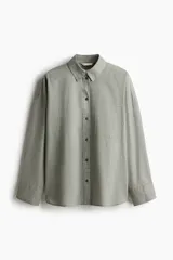 Camisa verde claro de lino y algodón, corte amplio, con cuello clásico, cierre frontal con botones, bolsillo de parche en el pecho, mangas largas con puños abotonados y bajo redondeado con aberturas laterales.