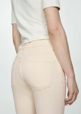 Pantalón de jean color crema, de corte flare y tiro alto, con cinco bolsillos y ruedo desflecado.