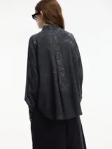 Camisa marrón con efecto acid wash, cuello camisero, corte recto y cierre frontal con botones.
