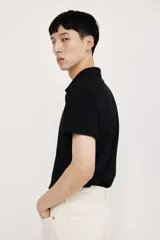 Remera polo negra de manga corta en piqué liviano de mezcla de algodón con cuello y tapeta de botones. Corte ajustado que realza el contorno del cuerpo creando una silueta entallada. Confeccionada con tejido funcional COOLMAX®, una fibra exclusiva de poliéster de secado rápido que elimina la humedad y regula la temperatura corporal proporcionando un ajuste cómodo y suave.
