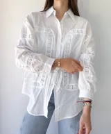 Camisa blanca de mangas largas con detalles de broderie en el frente, mangas y espalda. Corte recto, cuello clásico y cierre frontal con botones.