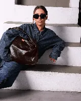 Bolso marrón oscuro de cuero sintético con forma ovalada y asa corta.